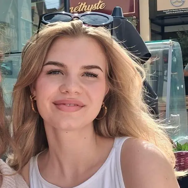Teamportrait Theresa Friseursalon München Ein junges Teammitglied mit blonden Haaren und weißem Tanktop lächelt in die Kamera vor einem Friseursalon in München.